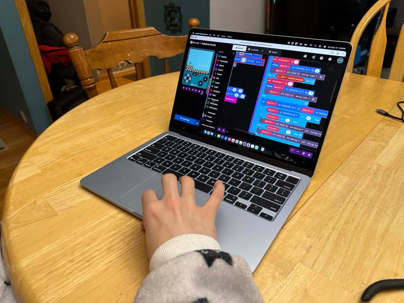 A computer with block code and a small video game next to it